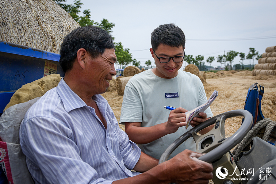 村民用農用三輪車將秸稈運送至臨時收儲點，小徐（右）給他們開單子計件。人民網記者 苗子健攝