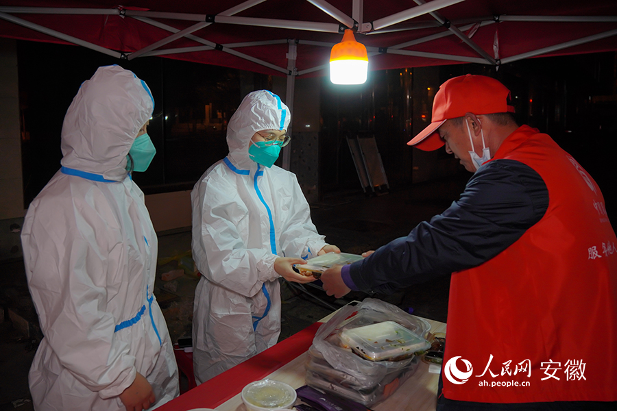 琥珀街道北苑村社区核酸检测采样点的志愿者将盒饭分给换班的“大白”。人民网 陈若天摄