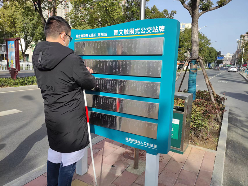 王湑正在触摸盲文公交站牌。六安市交通运输局供图