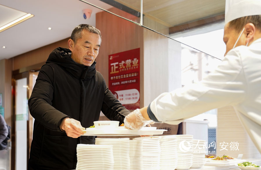 六安市鼓楼街道锥子庙社区居民李曙光正在食堂窗口前取餐。人民网 王锐摄