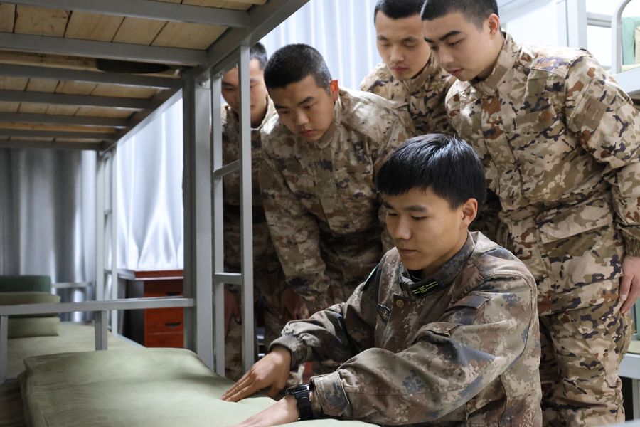 教练员在给预定新兵进行“豆腐块”叠被子培训指导。沈云鹏摄