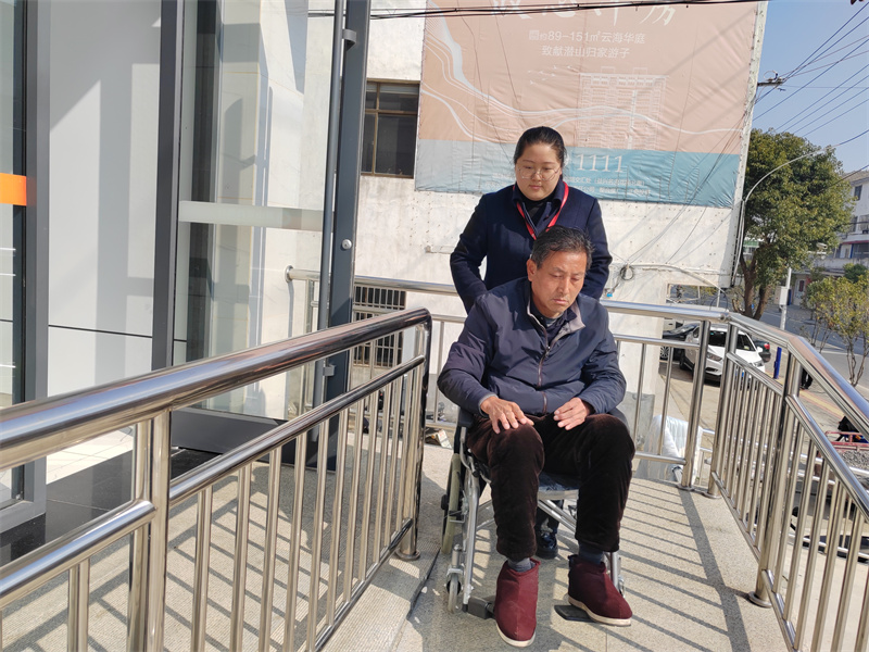 潛山農商銀行工作人員用輪椅接送行動不便老人。