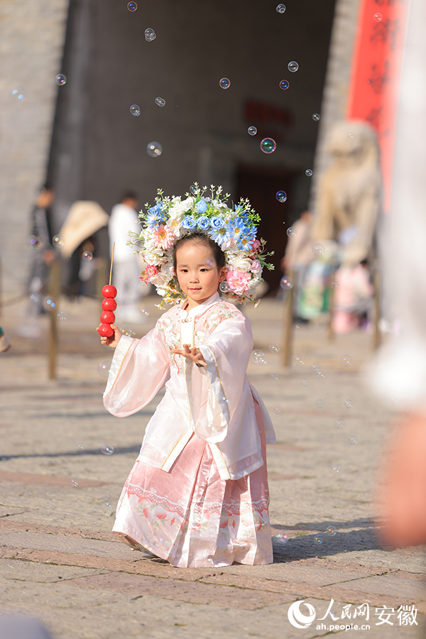一位頭戴簪花的小朋友在撮街上玩耍。人民網記者 王曉飛攝