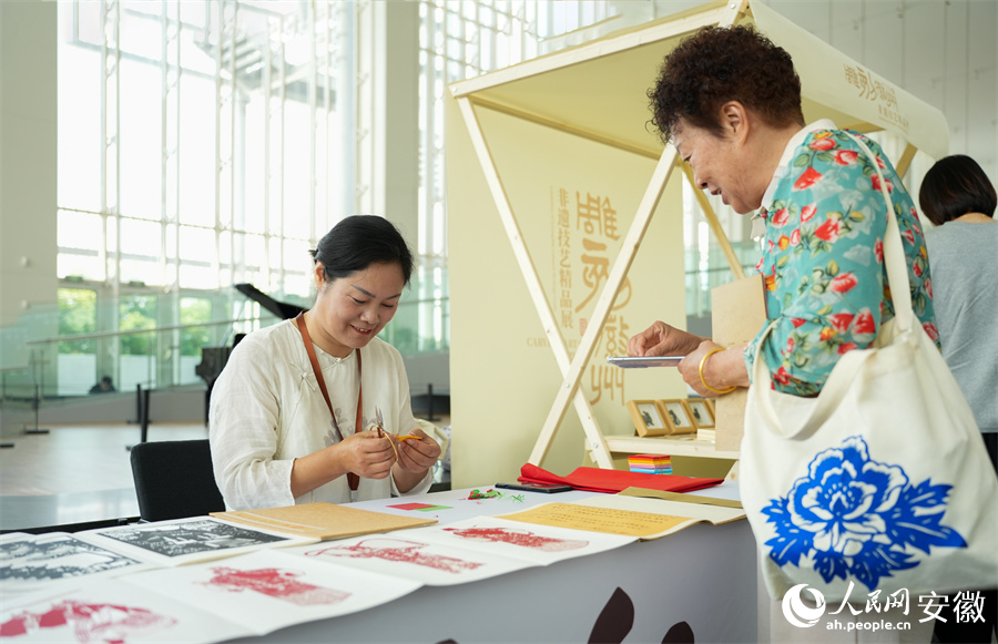 非遗传承人正同参观市民交流剪纸技巧。人民网记者 王锐摄