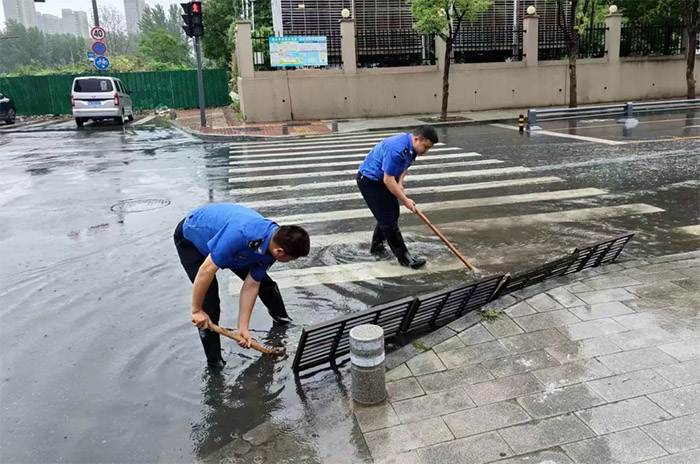 城管队员打开道路雨水篦子，加速路面积水排水。