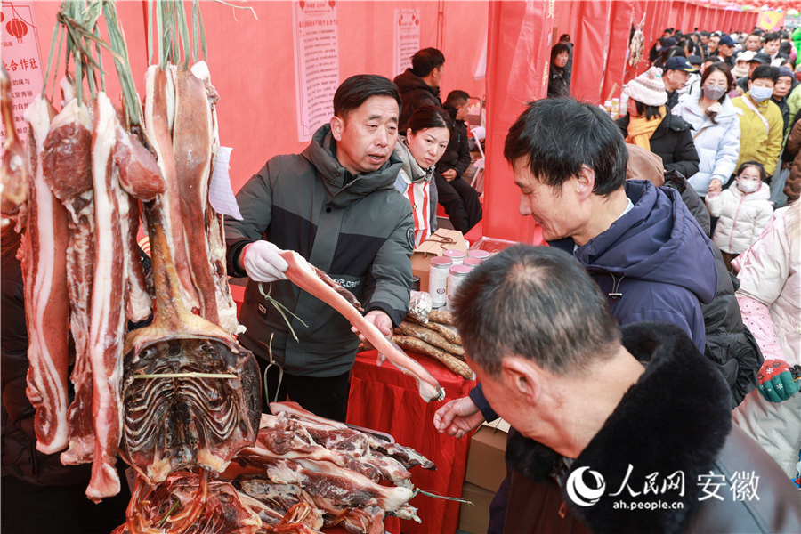 南陵年货集市现场，摊主向顾客推介自家生产的腊肉。人民网记者 张俊摄