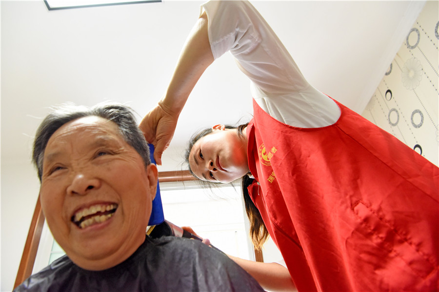 社区志愿者钱月娥（右一）为腰部摔伤的79岁陈凡珍老人上门义务理发。