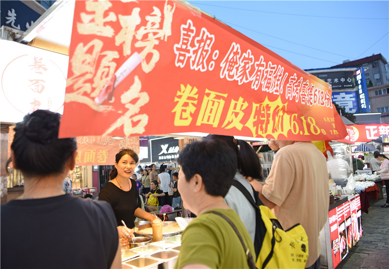 安徽省淮南市田家庵区商贸文化广场夜市，卷面皮摊主姚红艳让利消费者，与路人分享儿子高考好成绩的喜悦。