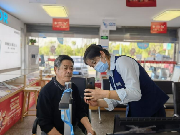 工作人员指导老年人进行手机面部识别操作。