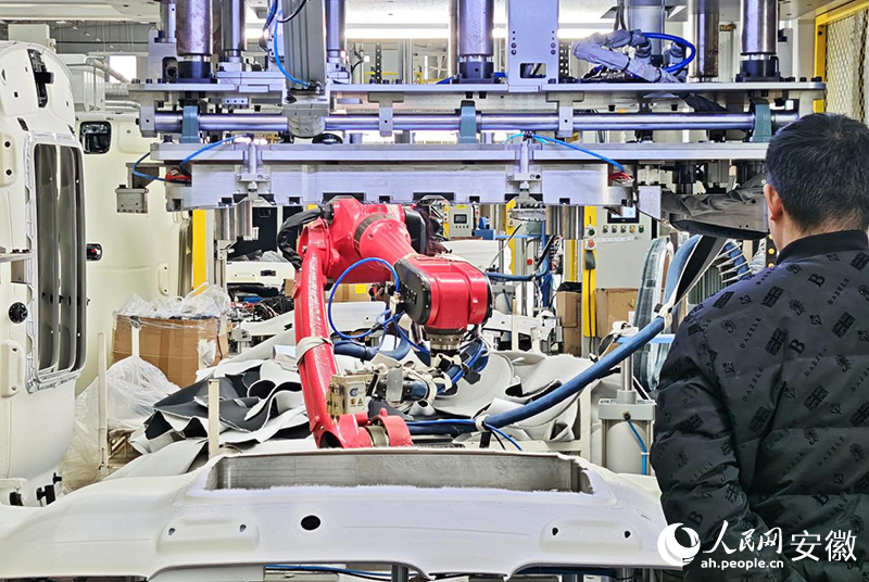 在吴圩镇一家汽车零部件企业里,工人正在看着机械臂加工零件。人民网记者 周坤摄