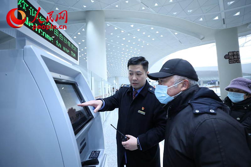 1月4日，在北京通州站，邵辰飛（左）幫助旅客使用自助購票機。人民網記者 尹星雲攝