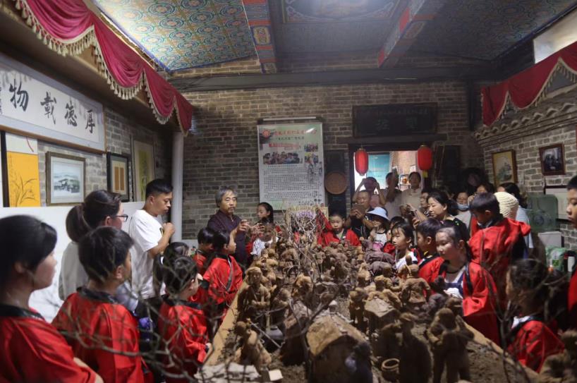 非遗工坊内，研学孩子围聚作品前，聆听代表性传承人讲解泥塑技艺。