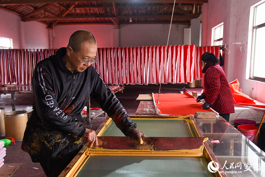工人正在使用丝网印刷工艺赶制“万年红”春联。人民网记者 李希蒙摄