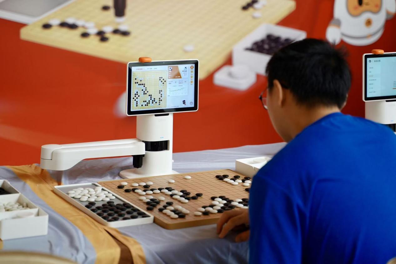 全国围棋定段赛外场，前来报道的小选手与围棋机器人对弈。淘云科技供图