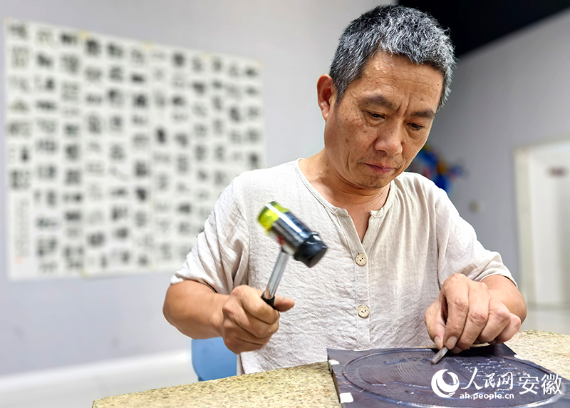 俯身案前敲铜拓画的魏贤洋。人民网记者 汪瑞华摄